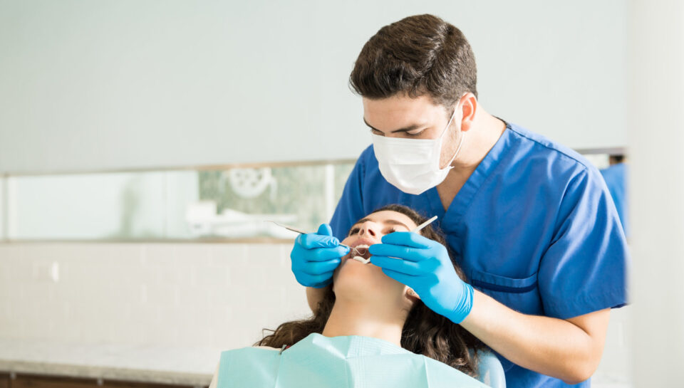Male dentist examining young woman with dental carver at medical clinic